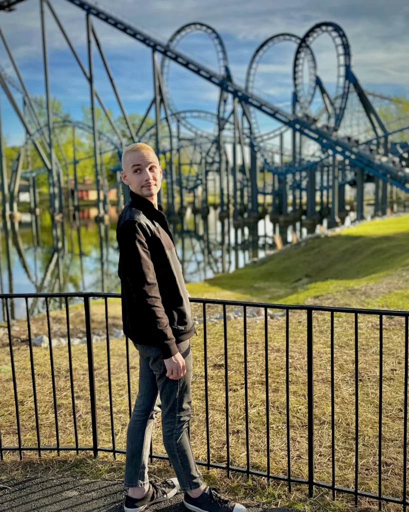 Light skinned man looking over shoulder in front of Blue Hawk roller coaster at Six Flags Over Georgia