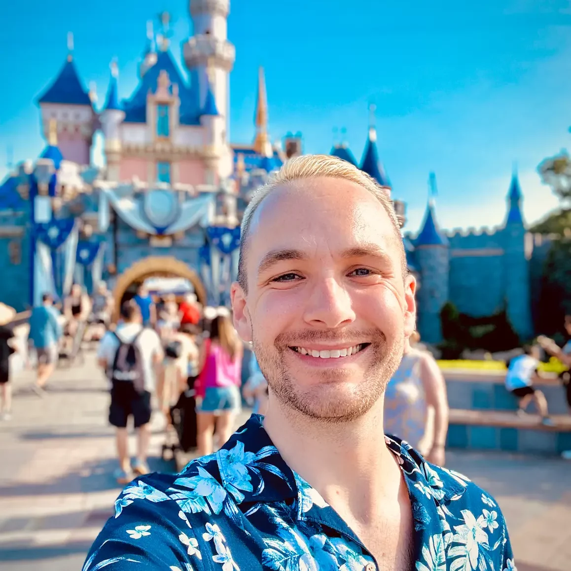 Light skinned man smiling for selfie in front of Snow White's castle at Disneyland 