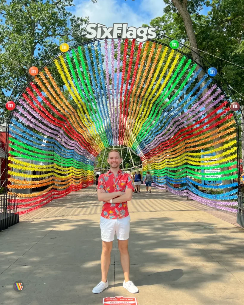 Light skinned man, Christian from Vertigo Views, standing in front of rainbow M&M streamers tunnel at Six Flags Great Adventure
