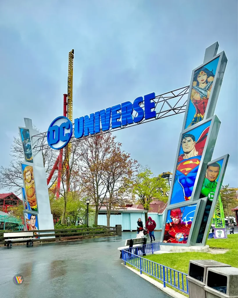 DC Universe Sign with The Flash: Vertical Velocity tower behind it on a cloudy day at Six Flags Great America