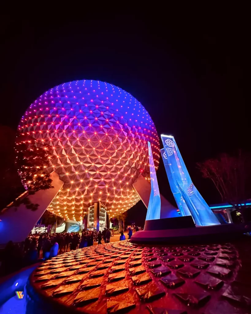 Spacehip Earth at night behind the EPCOT fountain. Both are lit in bright colors.