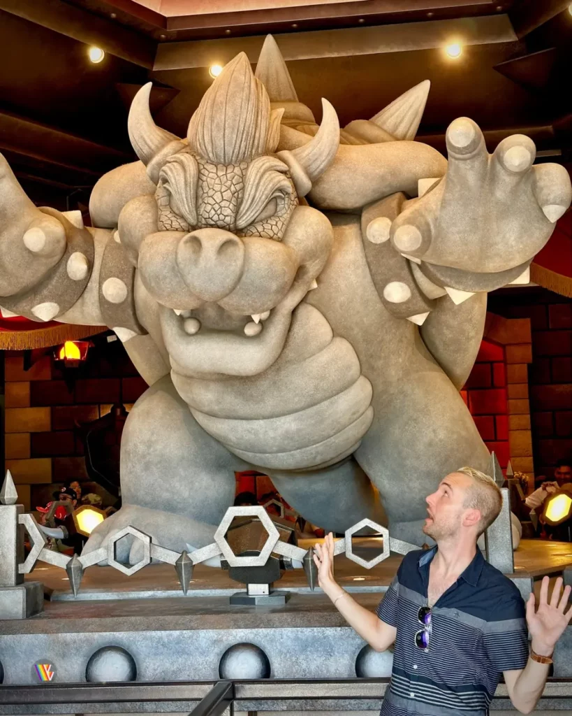Christian McIlwain standing next to giant statue of Bowser inside queue of Mario Kart Bowser's Challenge at Universal Studios Hollywood