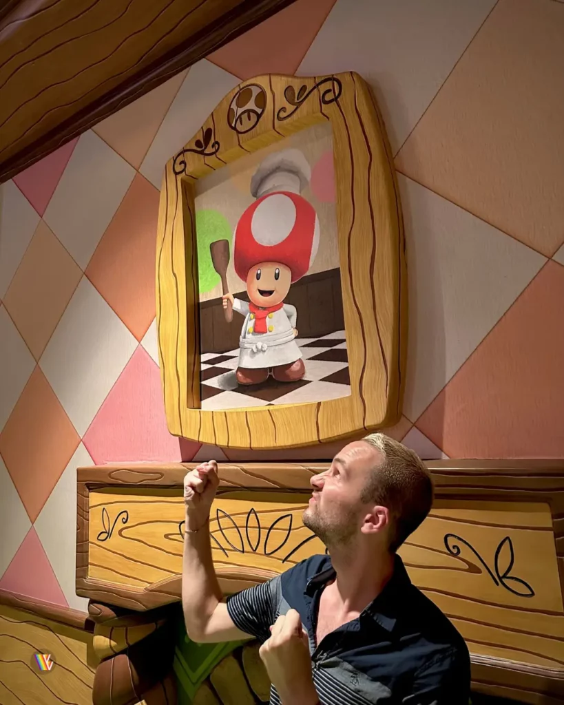 Christian McIlwain standing angrily and getting ready to throw hands next to fireplace with portrait of Toad above it in Toadstool's Cafe at Universal Studios Hollywood